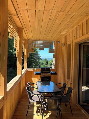 Eine Holzterrasse mit Grill, Tisch und Stühlen, mit Blick auf eine malerische Landschaft.