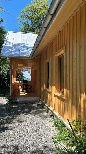Eine Holzhütte mit überdachter Terrasse, Grill und einem Schotterweg.