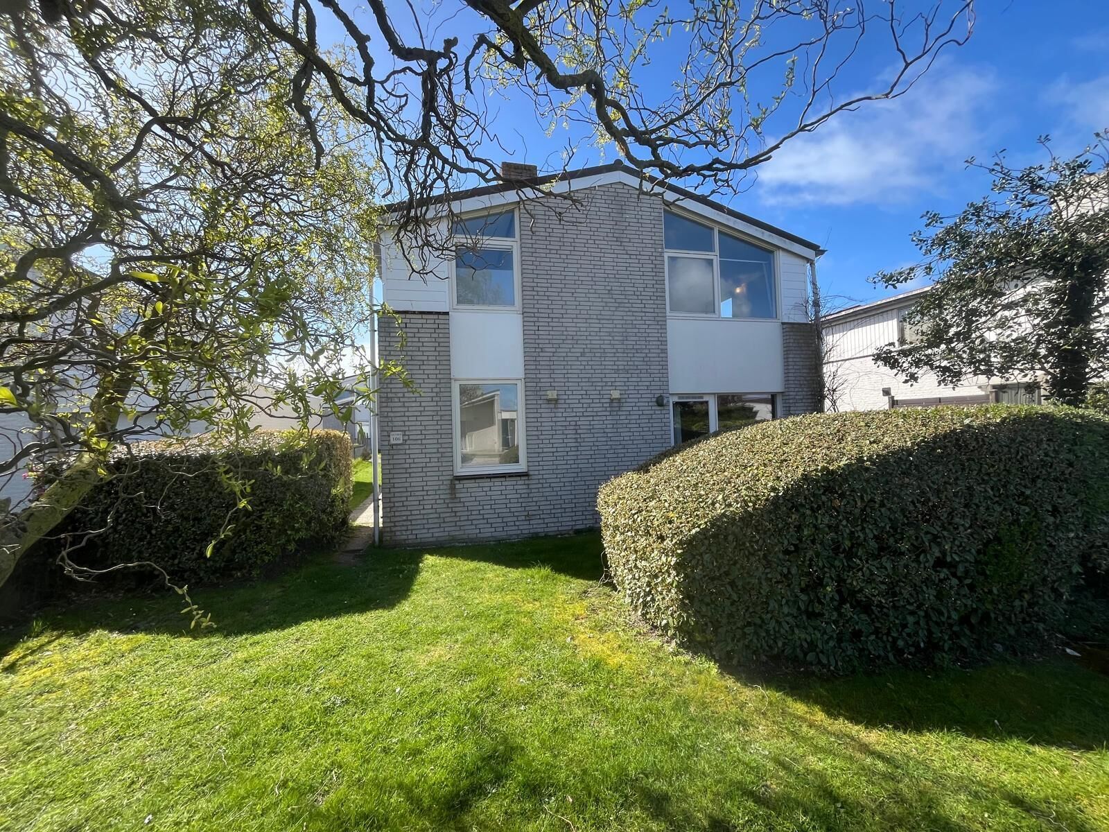 Une maison moderne à deux étages, dotée d’une façade en briques, de grandes fenêtres et d’une pelouse bien entretenue.