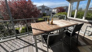 Um deck de madeira com uma mesa e cadeiras, uma garrafa de vinho e um copo sobre a mesa.