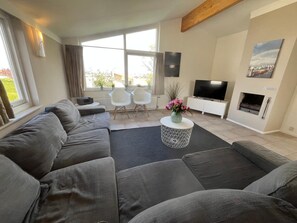 Ein modernes Wohnzimmer mit einem großen grauen Sofa, einem Flachbildfernseher, einem Kamin und einem großen Fenster mit Vorhängen.