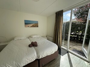 A bedroom with a bed, a painting of a beach, and a view of a garden through a glass door.