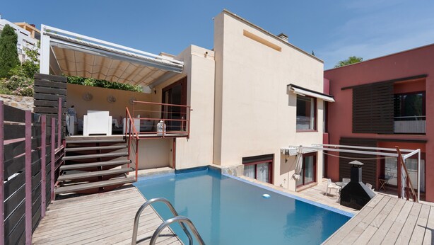 Una piscina con muelle de madera, escalera metálica y zona cubierta con escalones que conducen a un edificio.