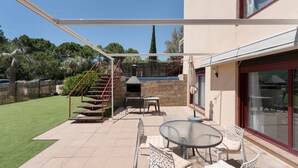 Un patio con mobiliario exterior, una chimenea de piedra y una escalera que lleva a un área cubierta.
