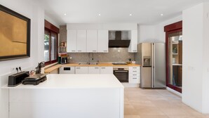 Una cocina moderna con armarios blancos, una isla central, electrodomésticos de acero inoxidable y un ventanal grande.