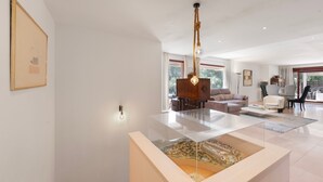 Una sala de estar moderna con una mesa de centro de vidrio, un aparador de madera y una lámpara colgante.