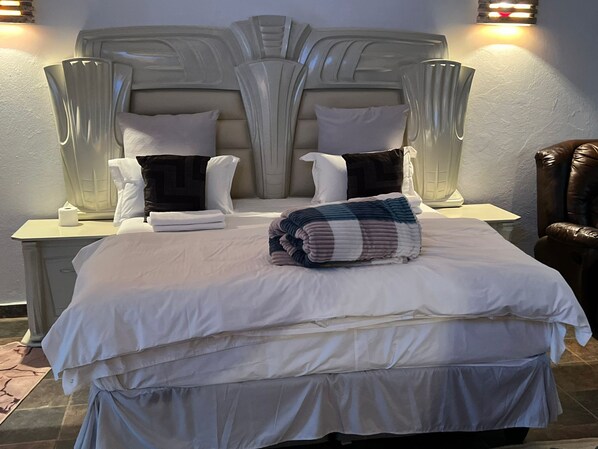 A neatly made bed with white linens, a folded blanket, and two pillows. There are two bedside tables with lamps and a brown leather chair. - One love suites (Mokopane)