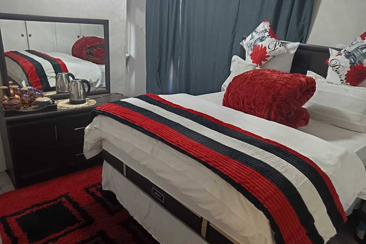 Habitación de hotel con cama, cómoda, espejo y una alfombra roja.