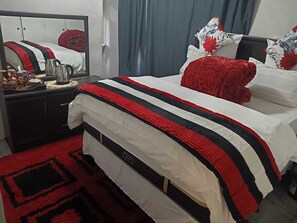 A hotel room with a bed, a dresser, a mirror, and a red rug. - One love suites (Mokopane)