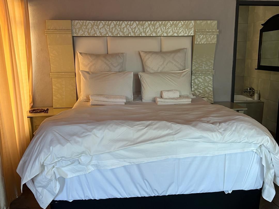 A hotel room with a large bed, a headboard with a patterned design, and a nightstand with a lamp and a phone.