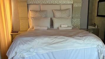 A hotel room with a large bed, a headboard with a patterned design, and a nightstand with a lamp and a phone.