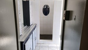 Een smalle gang die leidt naar een badkamer met een douche, betegelde wanden en een betegelde vloer.