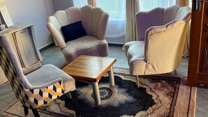 Een kamer met twee fauteuils, een klein houten tafeltje en een kamerkleed met een patroon.