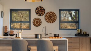 A modern kitchen with a central island, two chairs, a sink, and decorative plates on the wall. - Nomads Den - Safari Villa North - Private heated pool and riverbed views (Hoedspruit)