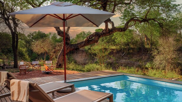 A poolside area with lounge chairs, a fire pit, and a large umbrella. - Nomads Den - Safari Villa North - Private heated pool and riverbed views (Hoedspruit)