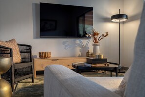 Ein modernes Wohnzimmer mit einer Couch, einem Sessel, einem Couchtisch, einem Fernseher, einer Stehlampe und einer Vase mit Trockenblumen.