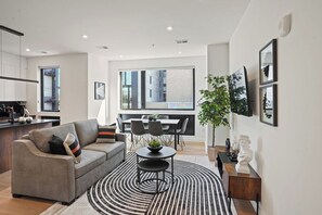 Una sala de estar moderna con un sofá, una mesa de comedor y sillas, una zona de cocina y un ventanal con vistas a la ciudad.