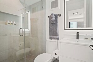 Un baño moderno con ducha de vidrio, inodoro, lavamanos con jabón de manos y un perchero para toallas.
