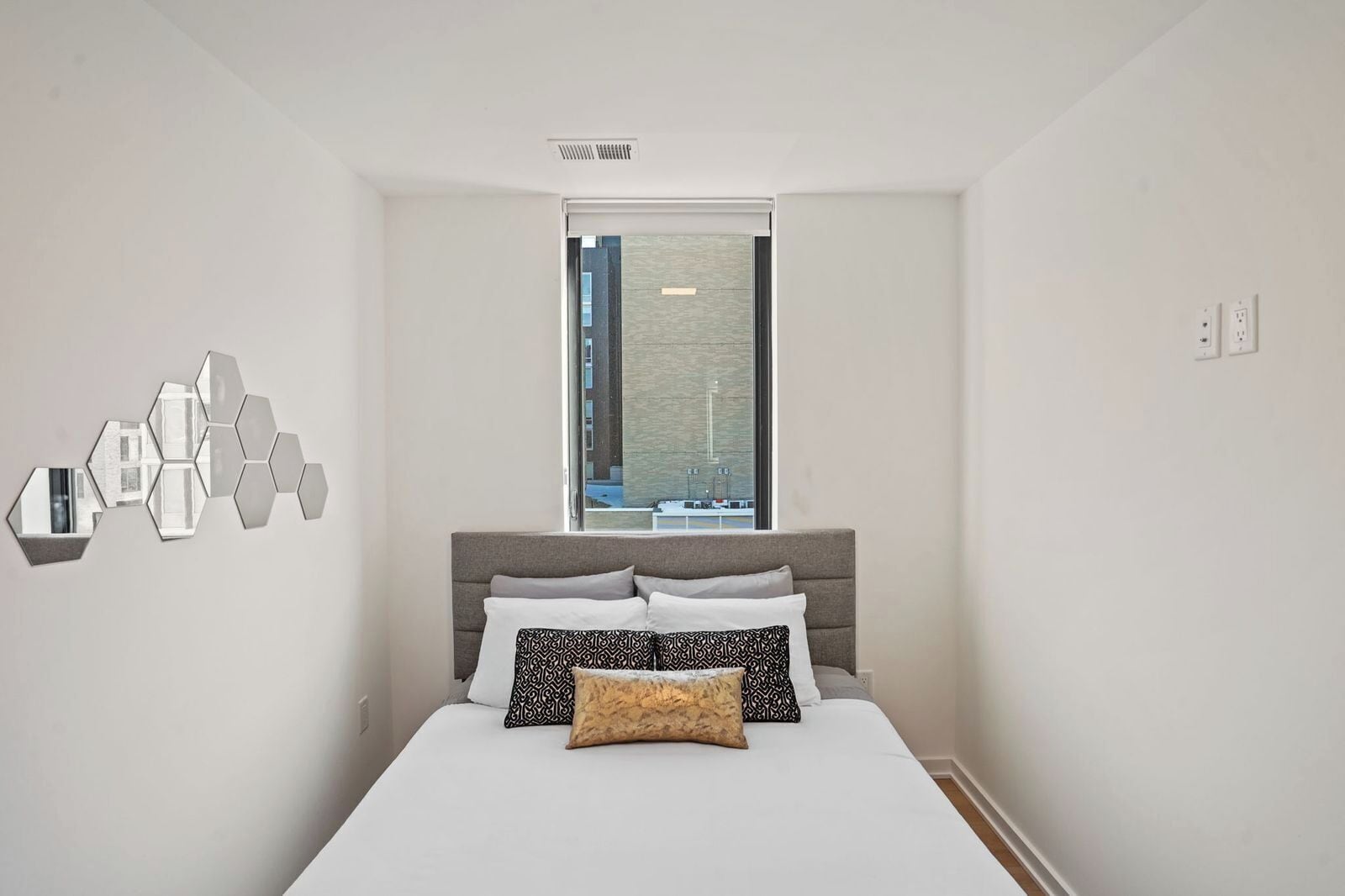 Ein Schlafzimmer mit Bett, Fenster, Wandspiegel und Deckenlüfter.
