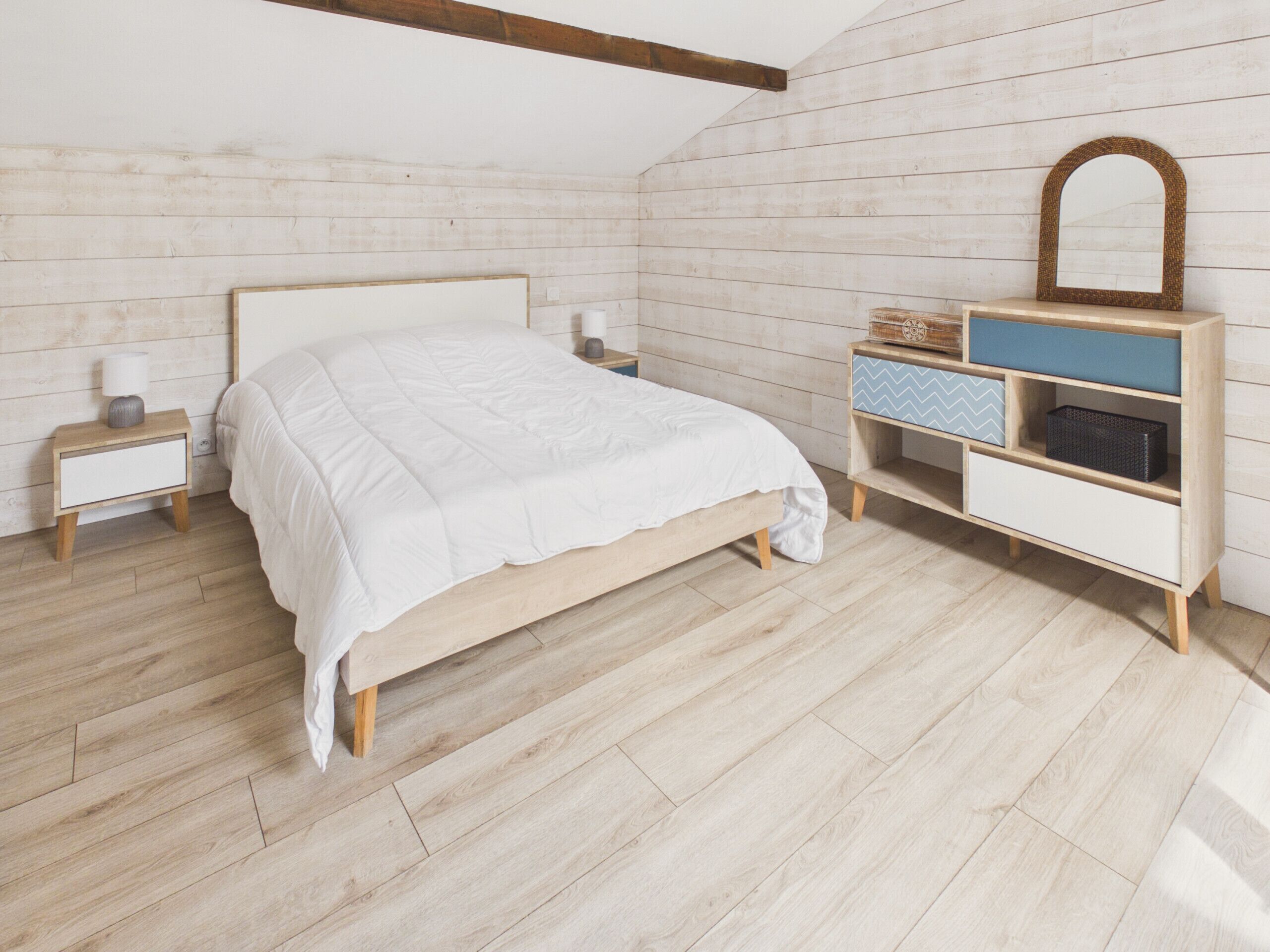 A bedroom with a wooden bed, a nightstand, a dresser with drawers, and a mirror.