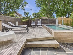 Una terraza de madera con sillones de descanso, una piscina pequeña y una zona con baldosas de piedra.