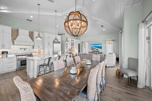 A spacious kitchen with white cabinetry, a large island, and a dining area with wicker chairs. - Casa Azul by Beach Boutique Rentals (Anna Maria)