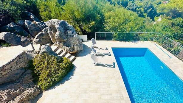 A swimming pool with a stone deck, lounge chairs, and a view of a forested hillside. - A stunning 4-bedroom home with swimming pool in Puerto Addaia, Menorca. (Port d'Addaia)