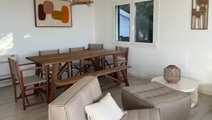 A dining area with a wooden table and chairs, a sofa, and a round white side table. - A stunning 4-bedroom home with swimming pool in Puerto Addaia, Menorca. (Port d'Addaia)