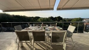 An outdoor dining area with tables and chairs, a view of the landscape, and a railing. - A stunning 4-bedroom home with swimming pool in Puerto Addaia, Menorca. (Port d'Addaia)