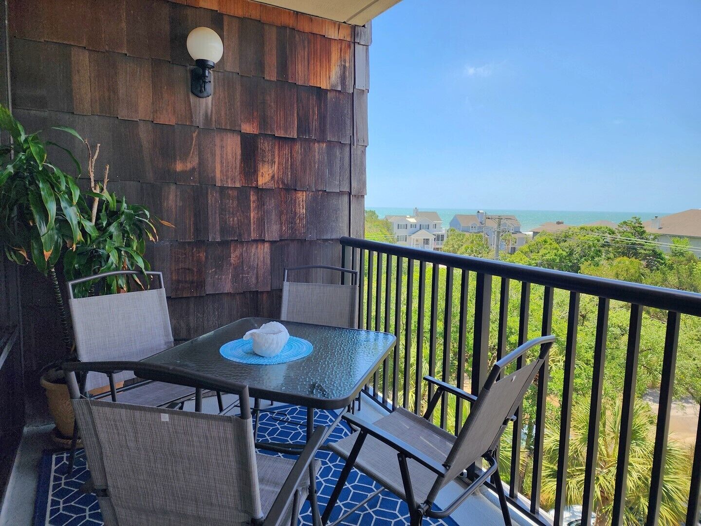 Un balcon avec une table et des chaises, un pot de fleurs et une vue sur l’océan et les maisons.