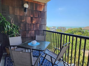 Ein Balkon mit Tisch und Stühlen, einem Blumentopf und Blick auf das Meer und Häuser.