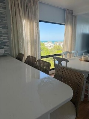 Ein Essbereich mit Tisch und Stühlen, Blick auf den Ozean und ein Balkon mit Vorhängen.