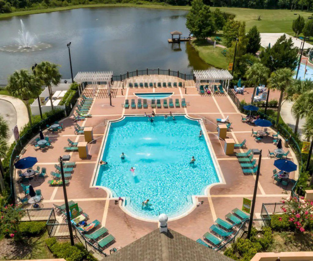 A large rectangular swimming pool with a surrounding deck, lounge chairs, and umbrellas.