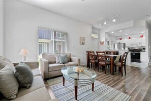 Ein modernes Wohnzimmer mit einem Glastisch, einer Couch und einem Essbereich mit Holzstühlen.