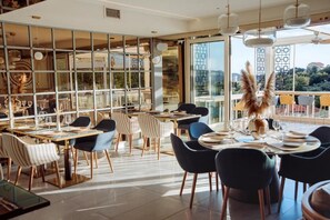 A modern dining area with multiple tables and chairs, large windows, and a view of the outdoors. - Status M Apartments 151 (Becici)