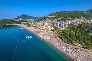An aerial view of a coastal city with a beach, buildings, and a mountainous backdrop. - Status M Apartments 151 (Becici)