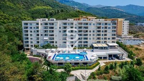A multi-story hotel with a swimming pool, surrounded by greenery and mountains. - Status M Apartments 151 (Becici)