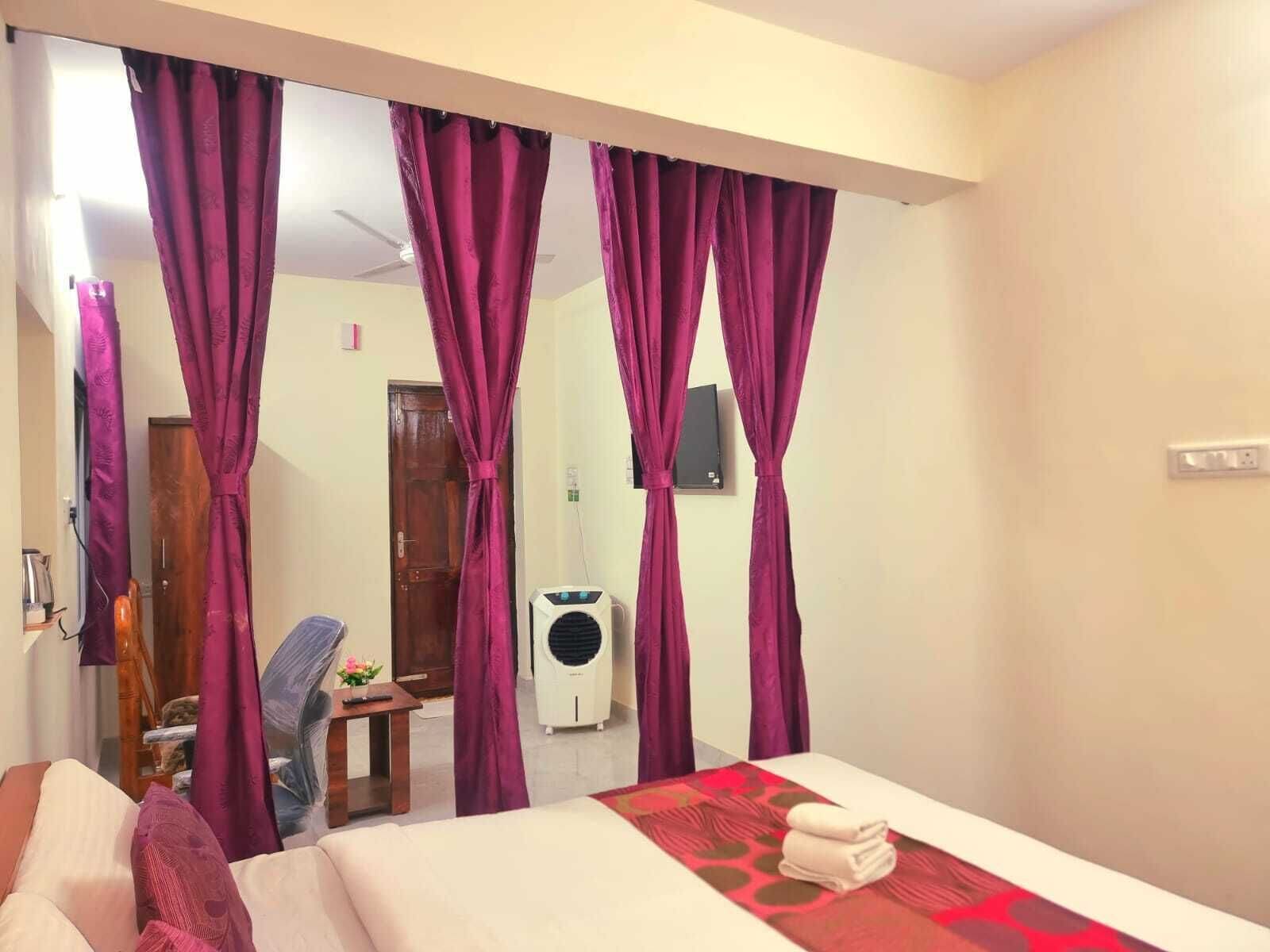 Una habitación de hotel con una cama, una mesita de noche, una silla, un espejo y cortinas moradas.