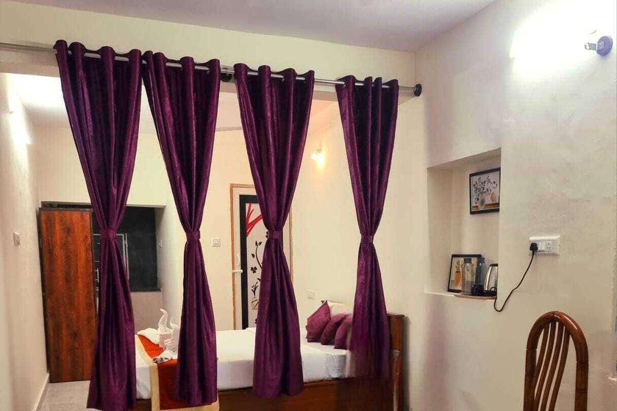 Una habitación con una cama, una mesa de madera, una silla y cortinas moradas.