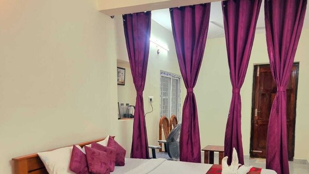 A bedroom with a wooden bed, purple curtains, a red blanket, and a small wooden nightstand. - The Green Homez (Bengaluru)