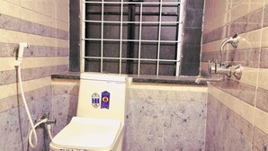 A bathroom with a toilet, a window with bars, and a bucket on the floor. - The Green Homez (Bengaluru)