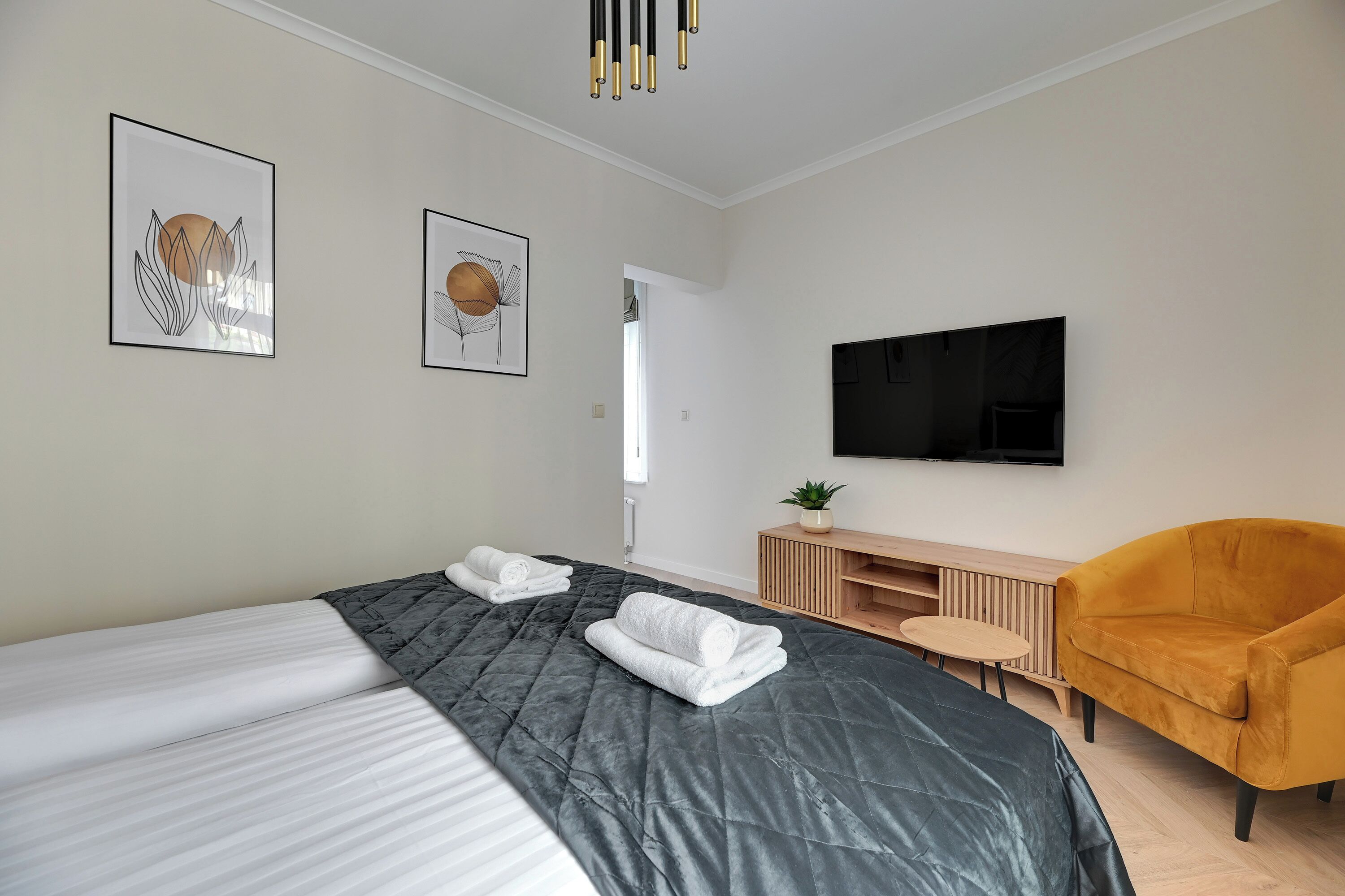 A modern hotel room with a large bed, a TV, a wooden side table, and a yellow armchair.