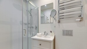 A bathroom with a glass shower enclosure, a white sink with a mirror above it, and a towel rack. - Sea & Monte City Center Apartments Sopot (Sopot)