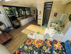 Una cocina moderna con un ventanal grande, un comedor con un tapete de colores y un pequeño balcón con plantas en macetas.