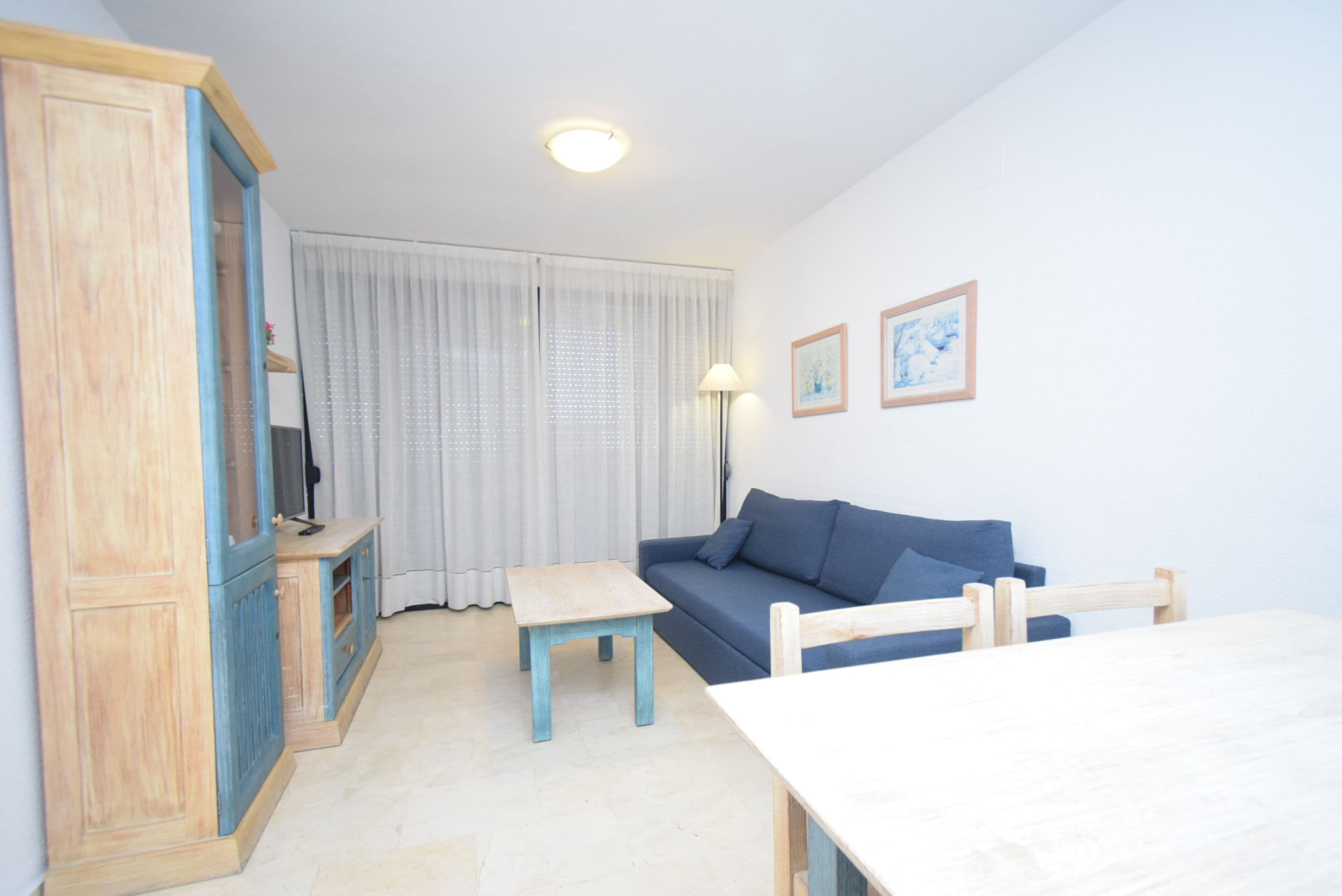 A room with a wooden cabinet, a blue sofa, a small table, and a white table.