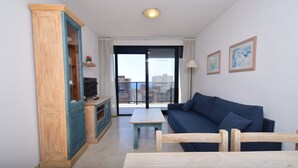 Ein Wohnzimmer mit einer Couch, einem Holztisch, einem Schrank und einem großen Fenster mit Blick auf die Stadt.