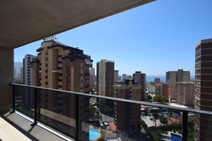Un edificio alto con varios balcones, cielo despejado y vista distante del mar.