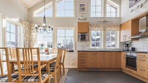 A modern kitchen with wooden cabinets, a dining area with a table and chairs, and large windows providing natural light. - Blåstöten - Ramundberget (Bruksvallarna)