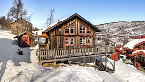 A wooden cabin with a balcony, a red door, and a snow-covered landscape. - Blåstöten - Ramundberget (Bruksvallarna)