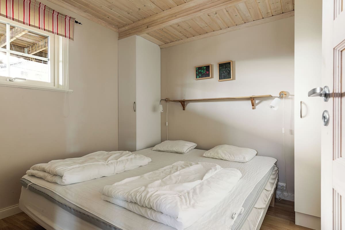 Een slaapkamer met een bed, een raam met gordijnen, een houten plafond en een deur.